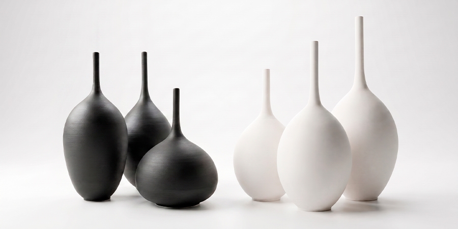 Colección de seis jarrones de cerámica de autor minimalistas con cuello largo, presentados en grupos de tres mates en negro y blanco sobre un fondo limpio.