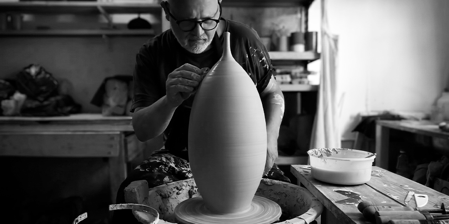 Fotografía en blanco y negro de Fernando Durão modelando con precisión el cuello de un jarrón de gres en el torno alfarero de su taller.