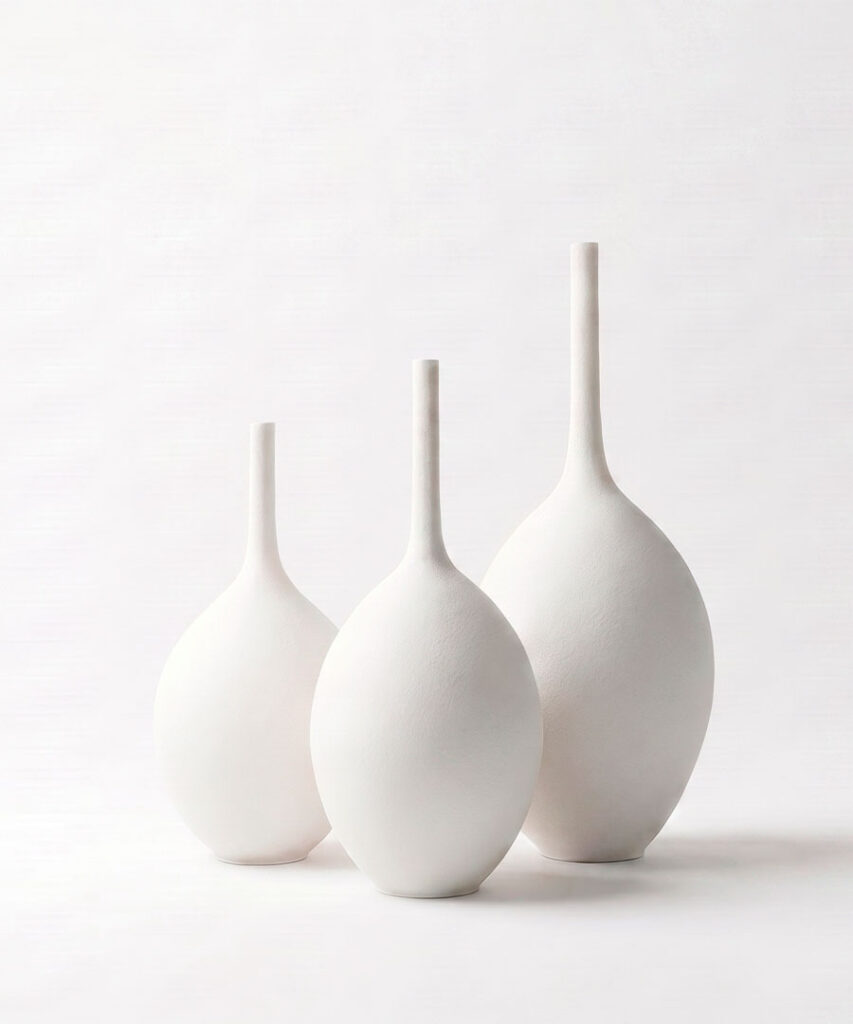 Trío de jarrones decorativos grandes de cerámica gres blanca artesanal con cuello estilizado sobre fondo neutro.