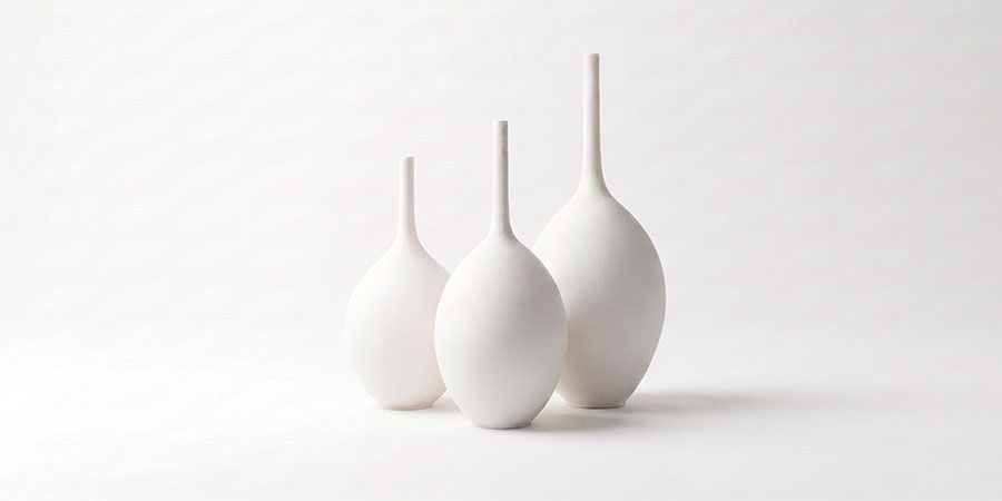 Trío de jarrones decorativos grandes de cerámica gres blanca artesanal con cuello estilizado sobre fondo neutro.